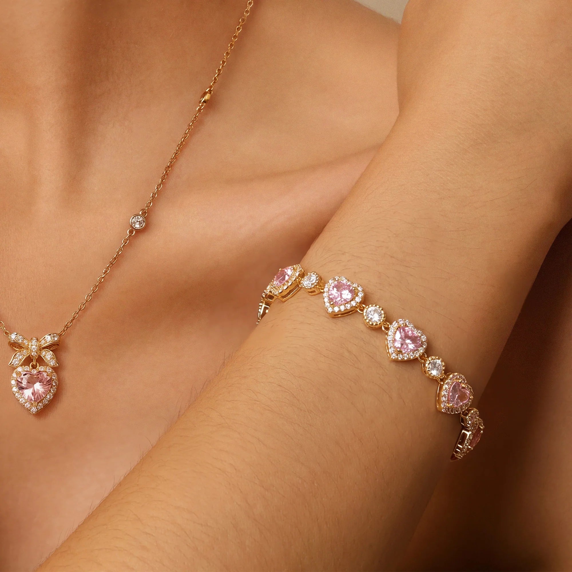 Gold-tone necklace and bracelet with pink stones and clear accents displayed on a model’s neck and wrist