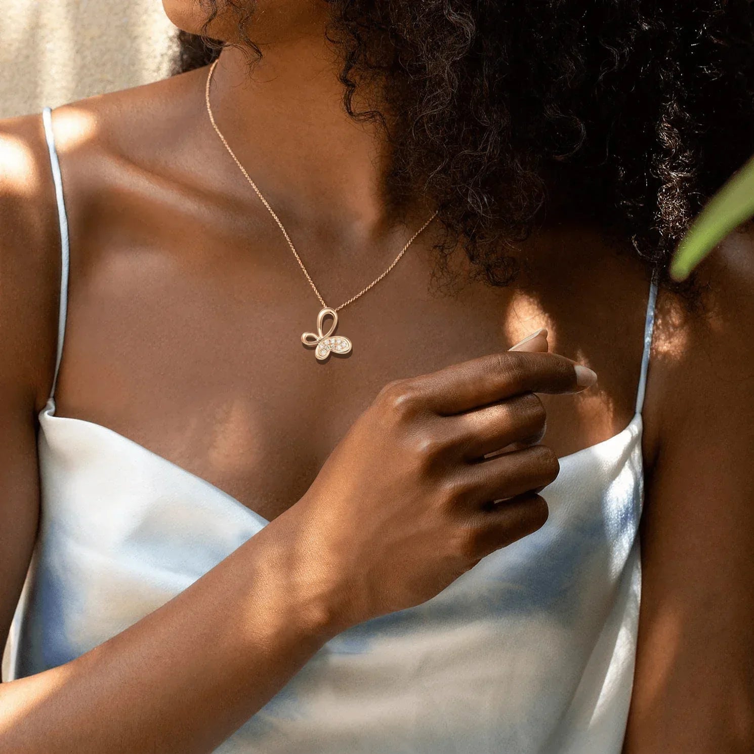 Butterfly pendant necklace worn on a person's chest in dappled sunlight.